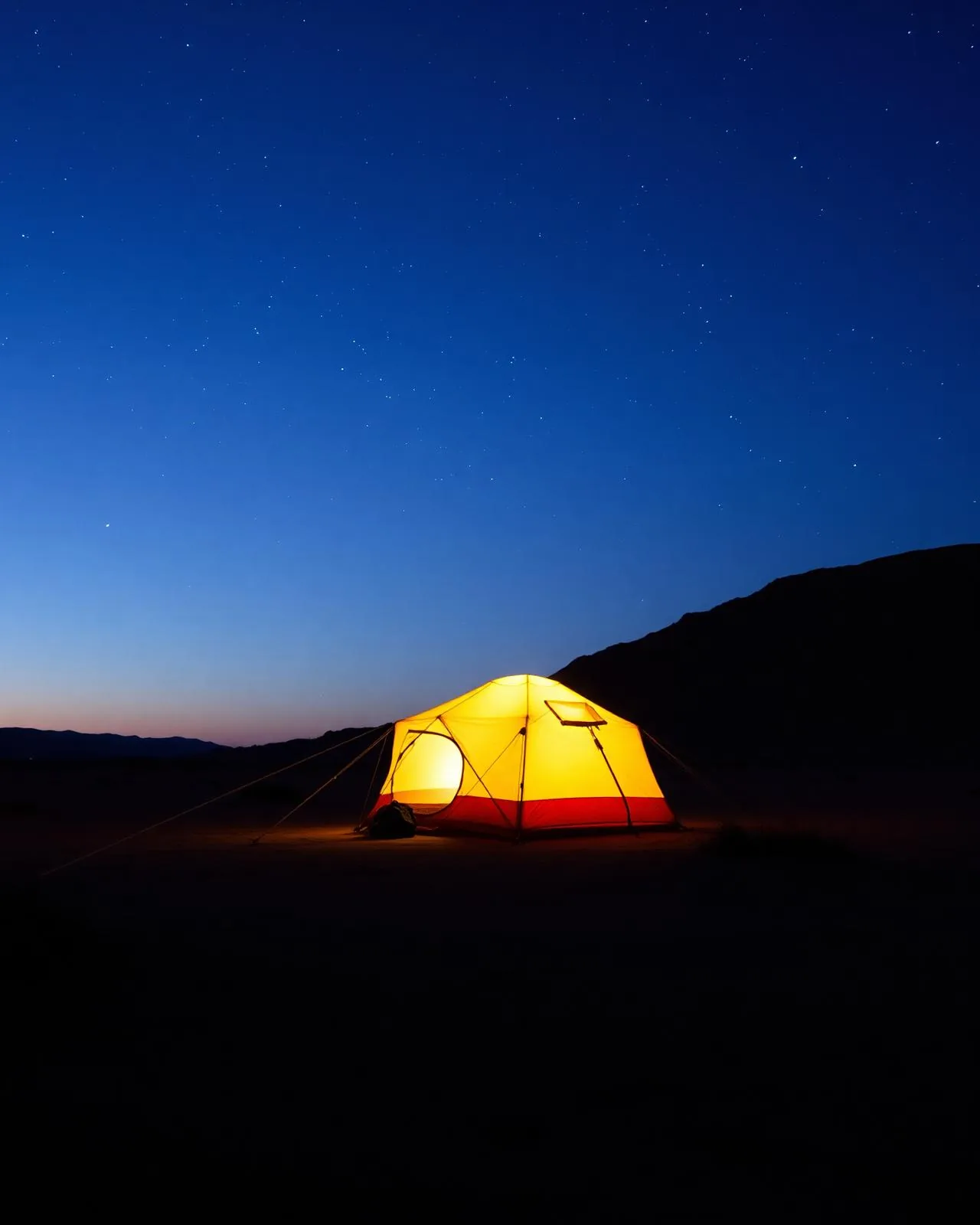 Lit tent under a starry desert sky